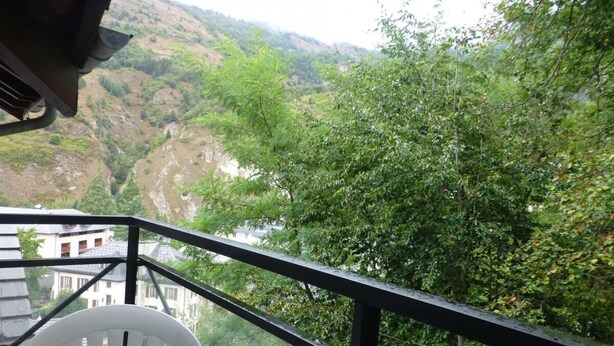 Un balcón con mesa y sillas con vistas a un valle con edificios y vegetación.