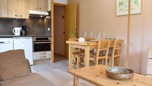 Una sala de estar acogedora con un sofá, una mesa de comedor de madera con sillas, y una zona de cocina con electrodomésticos.