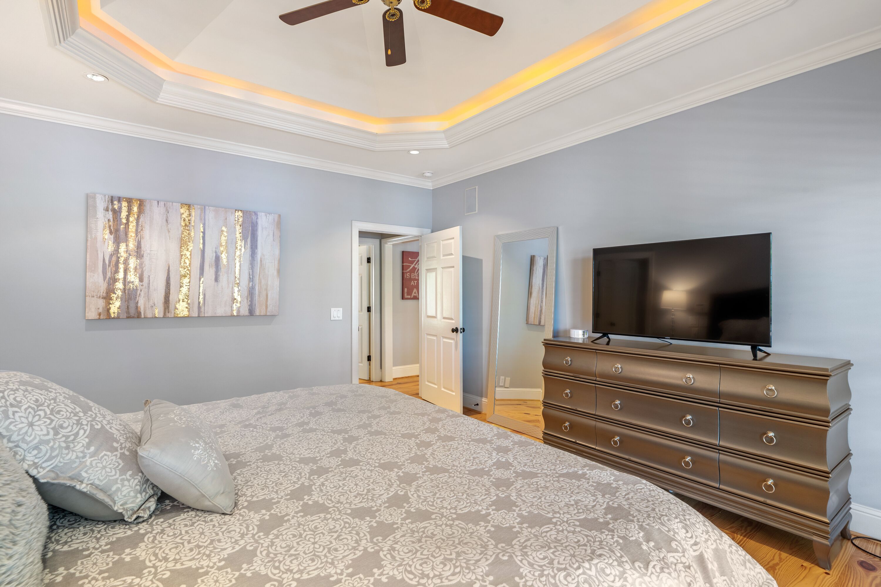 A bedroom with a large bed, a dresser, a flat-screen TV, and a ceiling fan.