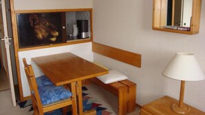 A compact room with a wooden table and bench, a small cabinet with a coffee maker, a mirror, and a lamp.