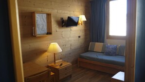 A cozy room with a wooden floor, a bed with blue bedding, a desk with a lamp, and a mounted TV.