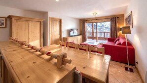 A wooden dining table with chairs, a red sofa, and a television in a room with wooden walls and a window with a view of mountains. - 100m from ski slopes, 3rd floor, balcony, parking, tv, 68m², Saint Martin de Belleville (Saint-Martin-de-Belleville)