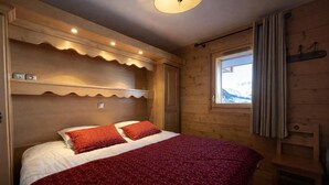 A cozy bedroom with a large bed, wooden headboard, and a window with curtains. - 100m from ski slopes, 3rd floor, balcony, parking, tv, 68m², Saint Martin de Belleville (Saint-Martin-de-Belleville)