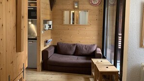 Une pièce chaleureuse avec un décor intérieur en bois, un canapé marron, une petite table et un coin cuisine visible à travers une porte ouverte.
