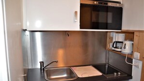Une cuisine compacte avec un évier en acier inoxydable, un four à micro-ondes et une machine à café placés sur une étagère en bois.