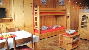 A wooden room with bunk beds, a table with fruit, a chair, and a small cabinet.