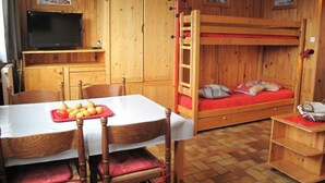 A wooden room with a bunk bed, a dining table with chairs, a TV, and wooden cabinets.