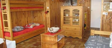 A wooden room with bunk beds, a cabinet with glass doors, and a small table.