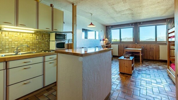 A kitchen with a central island, wooden cabinets, a microwave, and a window overlooking a mountainous landscape.