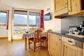 A kitchen with wooden cabinets, a Bosch oven, and a dining area with a table set for two. - 150m from resort center, 6th floor, view mountain/ski slopes, tv, 28m², Les Menuires (Les Menuires)