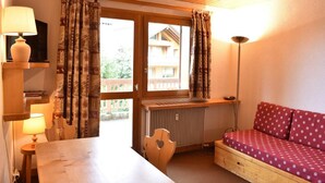 A cozy room with a wooden table, a red sofa with a patterned cover, a radiator, and a window with curtains. - 20m from ski slopes, 1st floor, swimming pool, balcony, tv, ski locker, 24m², Méribel (Méribel - Les Allues)