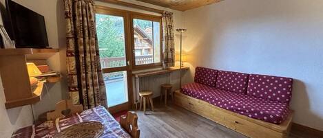 A cozy room with a wooden ceiling, a sofa with a patterned cover, a table with a woven basket, and a window with curtains.