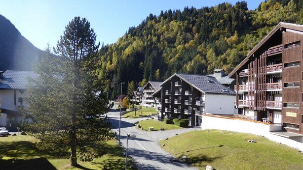 A resort with multiple chalet-style buildings, a central road, and a mountainous backdrop.