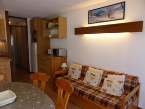 Een gezellige kamer met een houten bank, een eettafel en een keukenhoek met houten kasten en een magnetron.