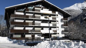 A multi-story hotel with balconies, set against a snowy mountain backdrop.