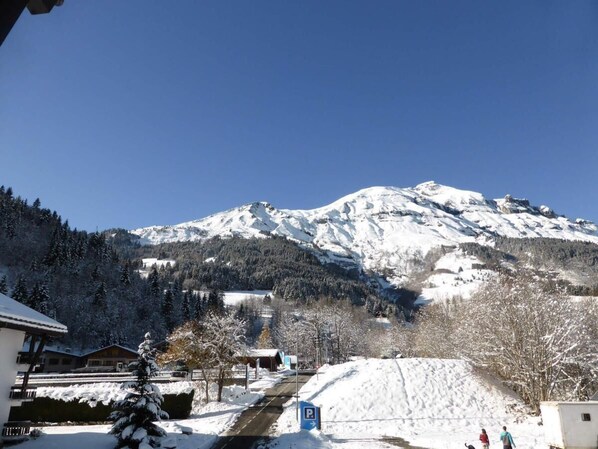 A snow-covered mountain with a clear sky, a road leading to a building with a parking sign, and a few people in the distance.