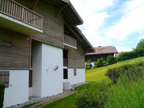 Una casa a due piani con un balcone, un vialetto in pietra e una collinetta erbosa sullo sfondo.