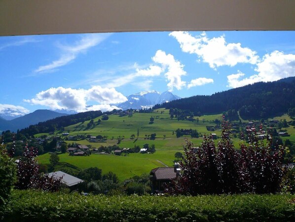 A rural landscape with rolling hills, scattered houses, and a mountain range in the background.