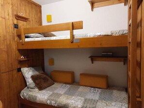 A bunk bed room with a wooden headboard, a small shelf, and a bedside table.