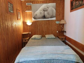A wooden-paneled room with a bed, two pillows, a nightstand, a lamp, and a framed picture on the wall. - 8th floor, view mountain, tv, 40m², Les Arcs (Les Arcs)