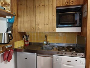 A compact kitchen with wooden cabinets, a microwave, a stove, and a dishwasher.