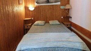 Une pièce aux murs lambrissés, avec un lit, deux oreillers, une table de chevet, une lampe et un tableau encadré accroché au mur.