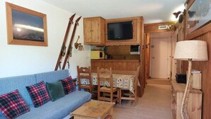 Un salon chaleureux avec un canapé bleu, des chaises en bois, une petite table en bois et un téléviseur fixé sur un meuble en bois.