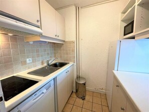 Een compacte keuken met een kookplaat, spoelbak en vaatwasser, met witte kastjes en een betegelde spatwand.