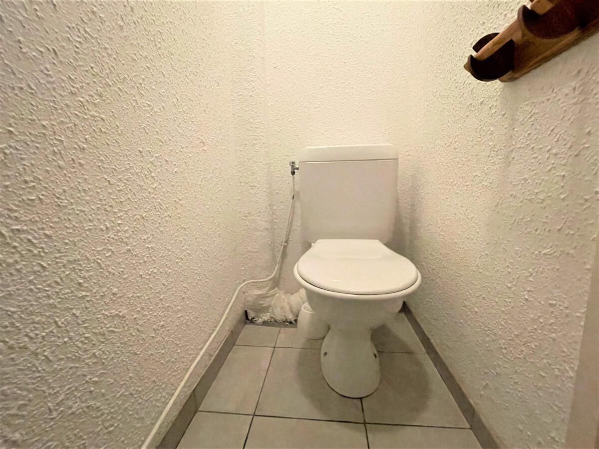 A small, white-tiled bathroom with a toilet and a wooden shelf above it.