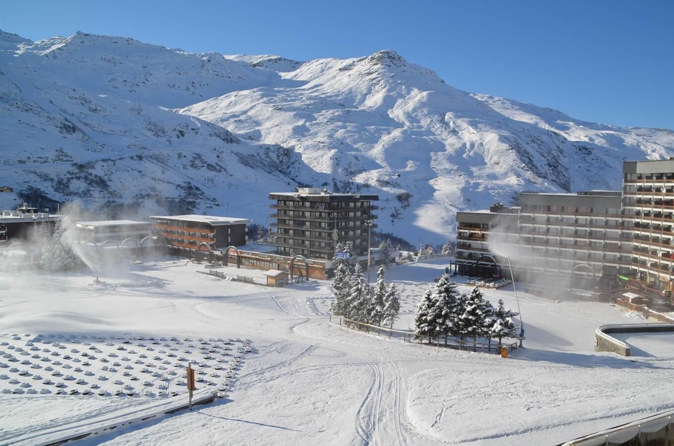 Ein schneebedecktes Gebirgsklima mit modernen Gebäuden, Skipisten und blauem Himmel.