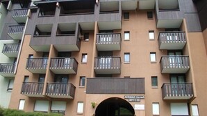 Een meerlaags appartementencomplex met balkons, een centrale ingang en een bord waarop staat dat het een appartementencomplex is.