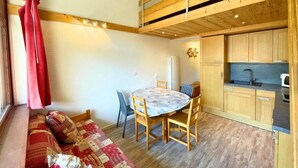 A cozy room with a wooden ceiling, a dining table with chairs, a sofa with patterned cushions, and a kitchenette with wooden cabinets. - 150m from ski slopes, view mountain, balcony, tv, 35m², Les Menuires (Les Menuires)