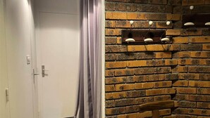 A room with a white door, a grey curtain, a brick wall, and a wooden bench.