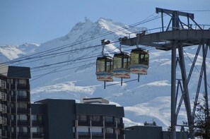 A cable car system with three gondolas, a mountain backdrop, and modern buildings in the foreground.