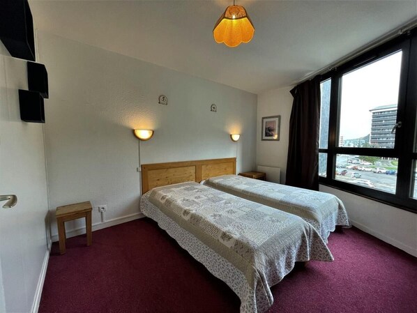 A room with two beds, a wooden headboard, a small table, and a window with a view of buildings.