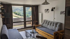 A cozy living room with a sofa, a small table, and a view of a mountainous landscape through large windows.