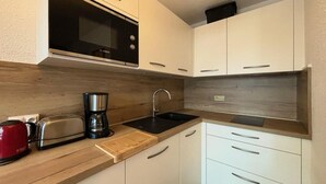 A compact kitchen with white cabinets, a wooden countertop, a Bosch microwave, a coffee maker, a toaster, and a red kettle.