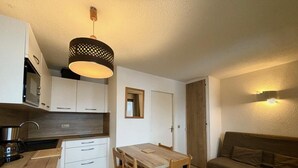 A compact kitchen with white cabinets, a wooden dining table, and a sofa.