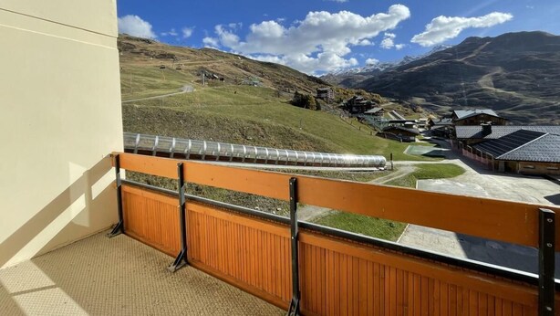 A balcony with a view of a mountainous landscape, a building with a sloped roof, and a clear sky.