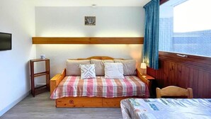 A cozy room with a bed, a small table, and a window with curtains. - 10m from ski slopes, 1st floor, balcony, tv, 17m², Les Menuires (Les Menuires)