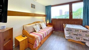 A cozy room with a wooden bed, a small bedside table, a TV, and a window with curtains. - 10m from ski slopes, 1st floor, balcony, tv, 17m², Les Menuires (Les Menuires)