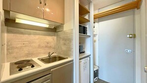 A compact kitchen with a stove, sink, and built-in oven. There is a microwave and a small refrigerator. A wooden shelf is above the sink. - 10m from ski slopes, 1st floor, balcony, tv, 17m², Les Menuires (Les Menuires)