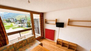 Una habitación con un ventanal grande, muebles de madera, un radiador rojo y un televisor montado.