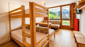 Una habitación con literas, un sofá, una mesa y vistas a las montañas.