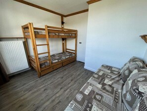 A room with a bunk bed, a sofa, and a radiator.