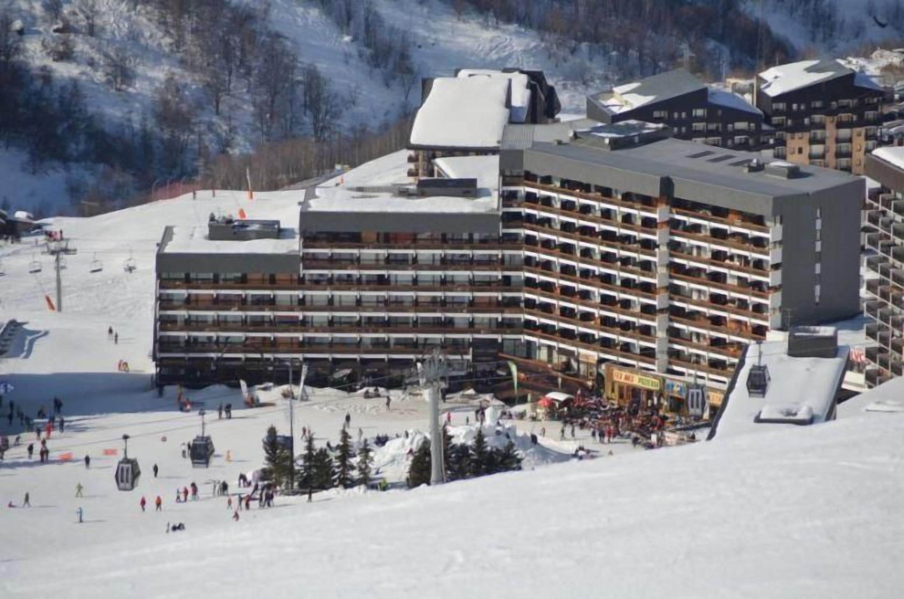 A multi-story hotel with balconies, located on a snowy slope with a ski lift in the background.