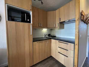 A compact kitchen with wooden cabinets, a built-in microwave, and a stainless steel sink.