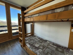 A bunk bed with a patterned mattress, a wooden ladder, and a window with a view of a mountainous landscape.