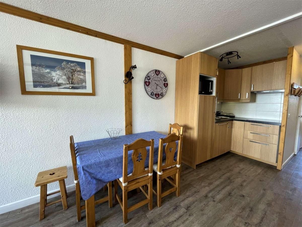 Cocina compacta con armarios de madera, microondas y un reloj en la pared.
