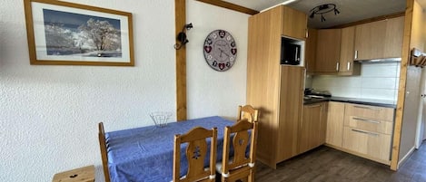 Cocina compacta con armarios de madera, microondas y un reloj en la pared.